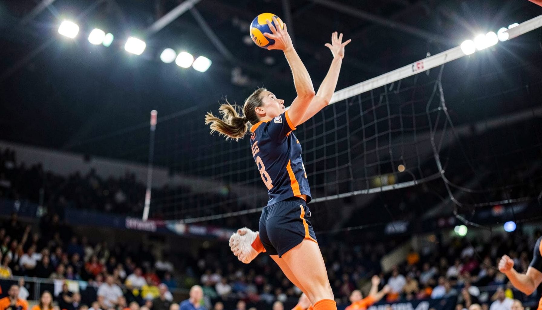 Volleyball player in a navy and orange jersey leaping for a spike under bright arena lights