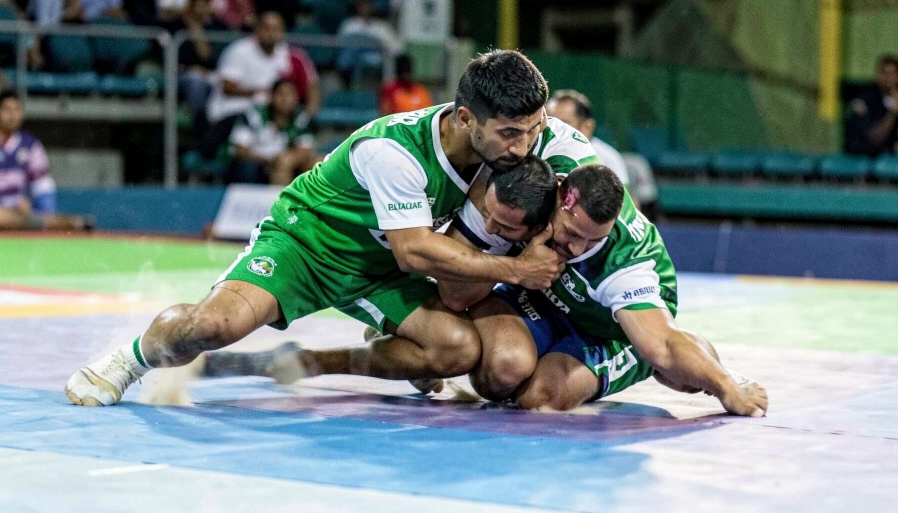 Kabaddi defender making a tackle, motion blur on the mat, bold green and white team colors