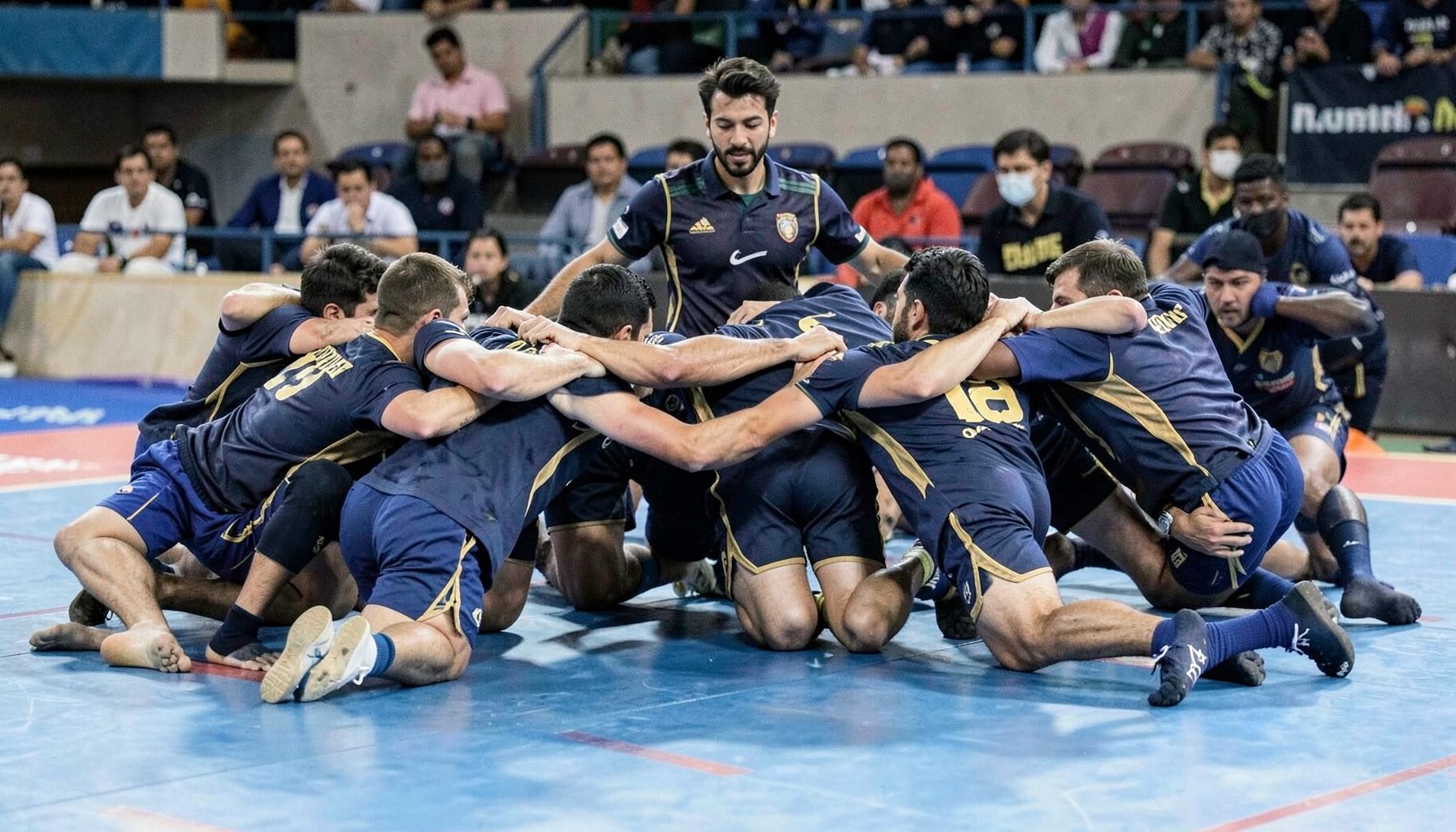 Kabaddi defenders forming a chain on the mat, arms locked, wearing dark blue and gold uniforms